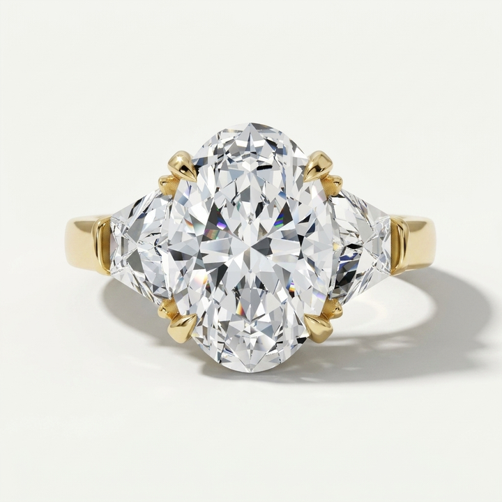 A three-stone diamond ring featuring a large oval center diamond in a yellow gold setting, flanked by two trapezoid-cut diamonds on a clean white background.