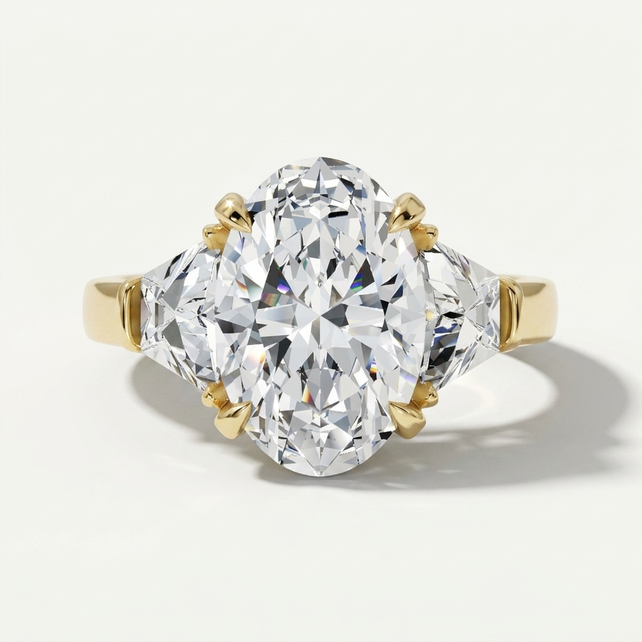 A three-stone diamond ring featuring a large oval center diamond in a yellow gold setting, flanked by two trapezoid-cut diamonds on a clean white background.