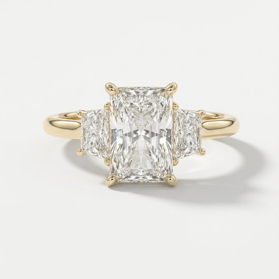 A radiant-cut three-stone diamond ring with a brilliant center stone and two smaller side stones set in a polished yellow gold metal band, shown on a light gray background.