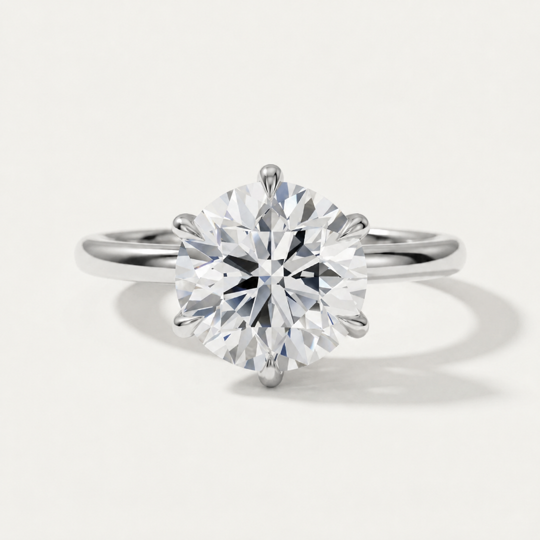 A classic solitaire engagement ring featuring a round brilliant-cut diamond set in a four-prong white gold band, photographed on a clean, light off-white background with a soft shadow.