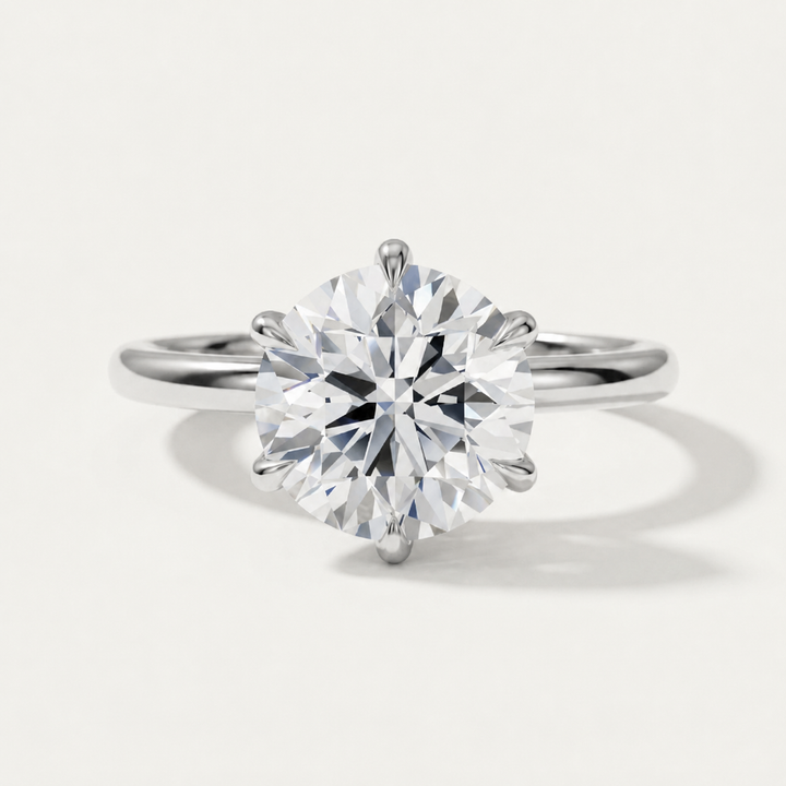 A classic solitaire engagement ring featuring a round brilliant-cut diamond set in a four-prong white gold band, photographed on a clean, light off-white background with a soft shadow.