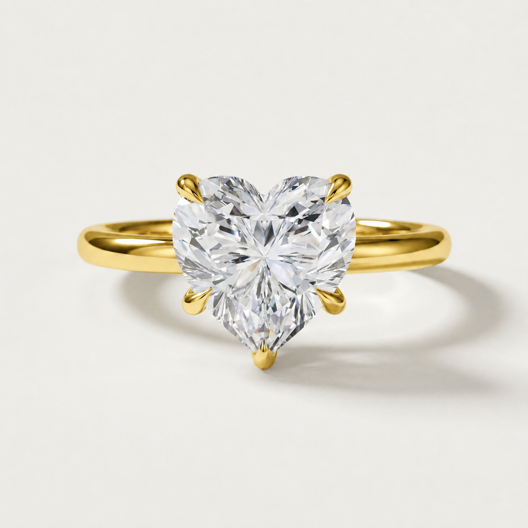 A heart-shaped diamond solitaire ring in a yellow gold setting, shown on a clean, light gray background.