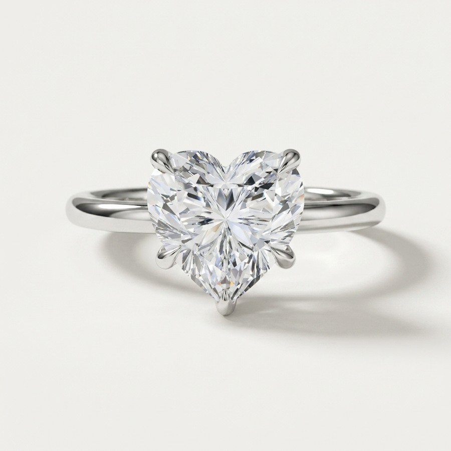 A heart-shaped diamond solitaire engagement ring in a White Gold metal band, set against a clean, light off-white background.