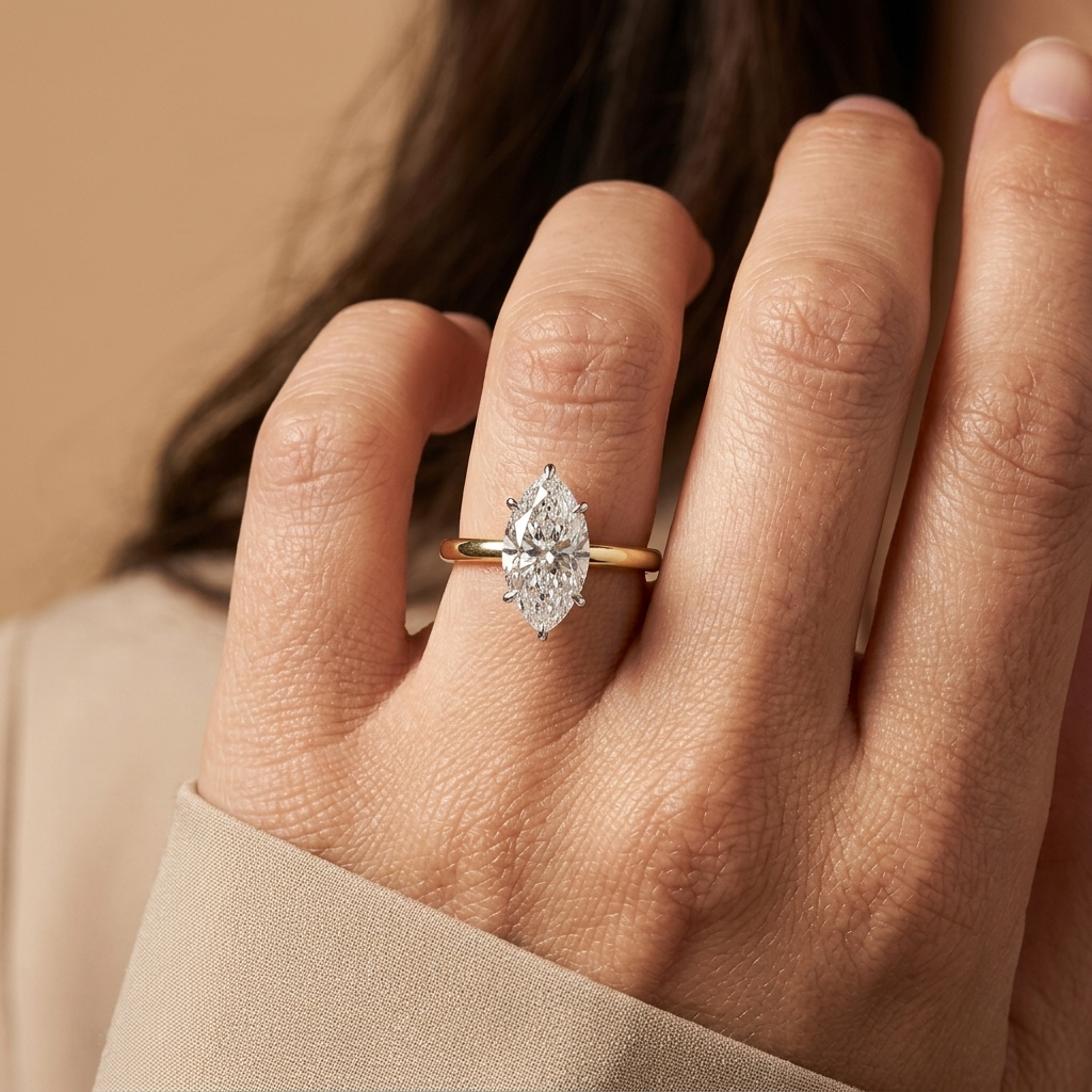 A close-up of a hand wearing a gold ring with a marquise-cut clear diamond, set against a soft beige background.