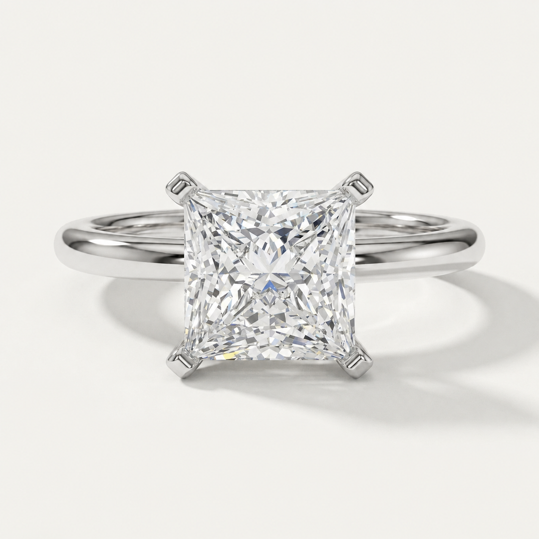 A princess cut diamond solitaire engagement ring in a polished white gold metal band, shown on a clean off-white background with a soft shadow.