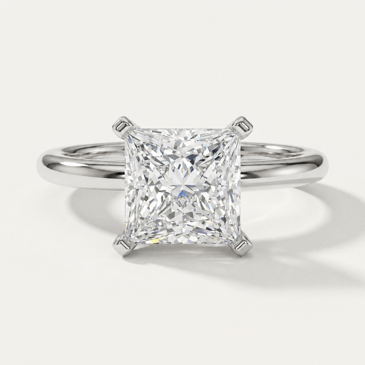 A princess cut diamond solitaire engagement ring in a polished white gold metal band, shown on a clean off-white background with a soft shadow.