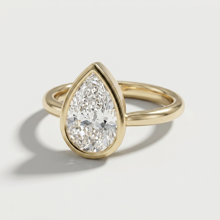A gold ring featuring a large pear-cut diamond in a teardrop-shaped bezel setting, shown on a light gray background with a soft shadow.