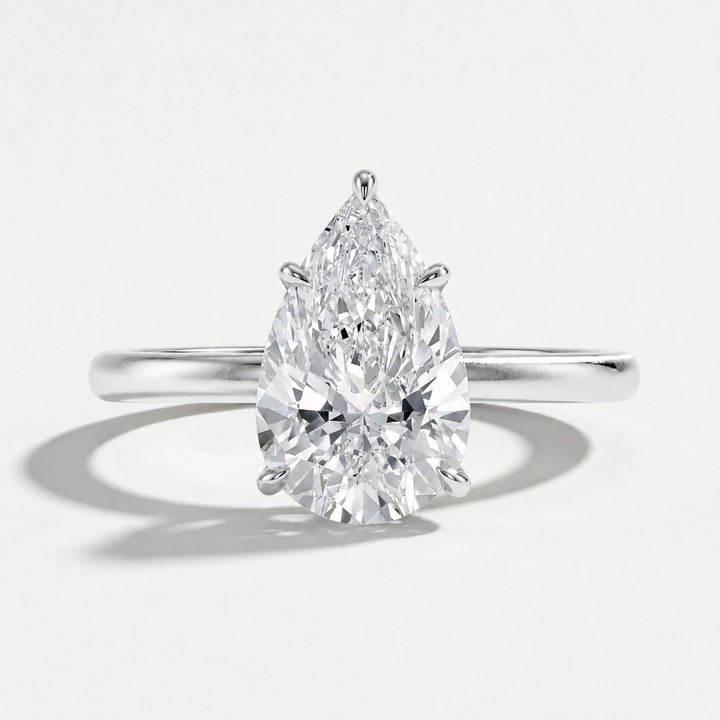 A pear-cut diamond engagement ring in a polished white gold or platinum band, shown on a clean light gray background with a soft shadow.