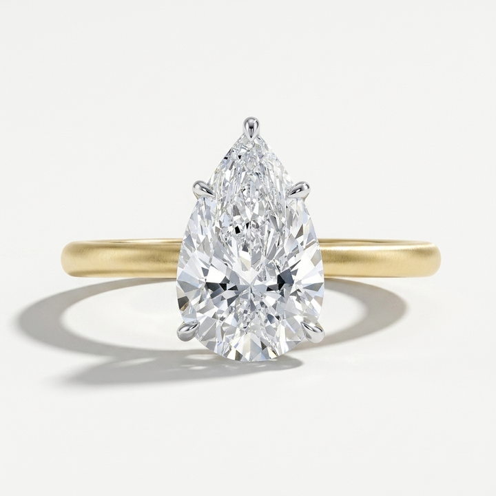 A pear-cut diamond engagement ring in a polished yellow gold band, shown on a clean light gray background with a soft shadow.
