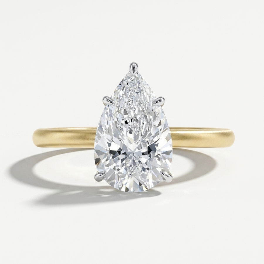 A pear-cut diamond engagement ring in a polished yellow gold band, shown on a clean light gray background with a soft shadow.