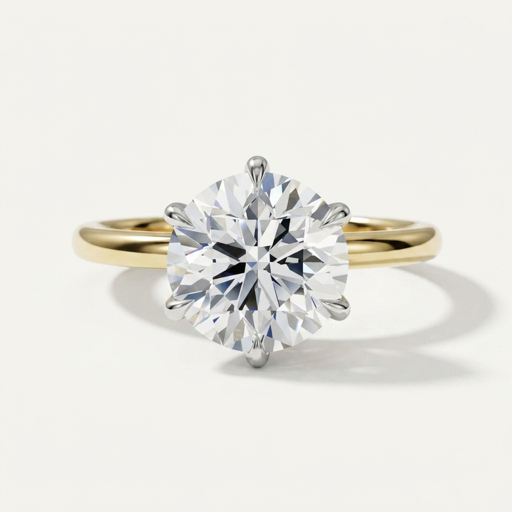 A classic solitaire engagement ring featuring a round brilliant-cut diamond set in a yellow gold four-prong band, photographed on a clean off-white background.