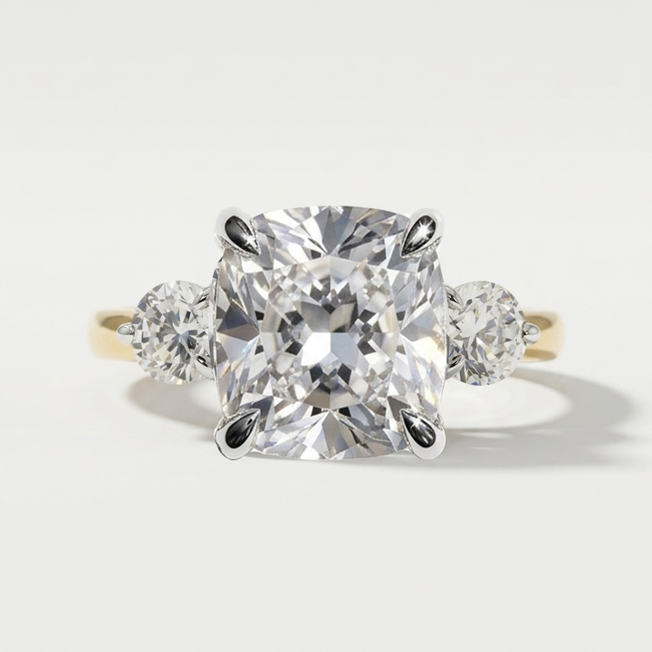 Three stone engagement ring with cushion center diamond and round side stones satin in a yellow gold band with white gold prongs