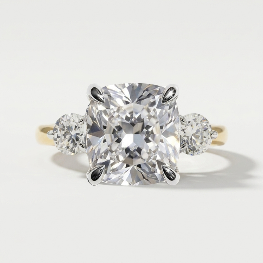 Three stone engagement ring with cushion center diamond and round side stones satin in a yellow gold band with white gold prongs