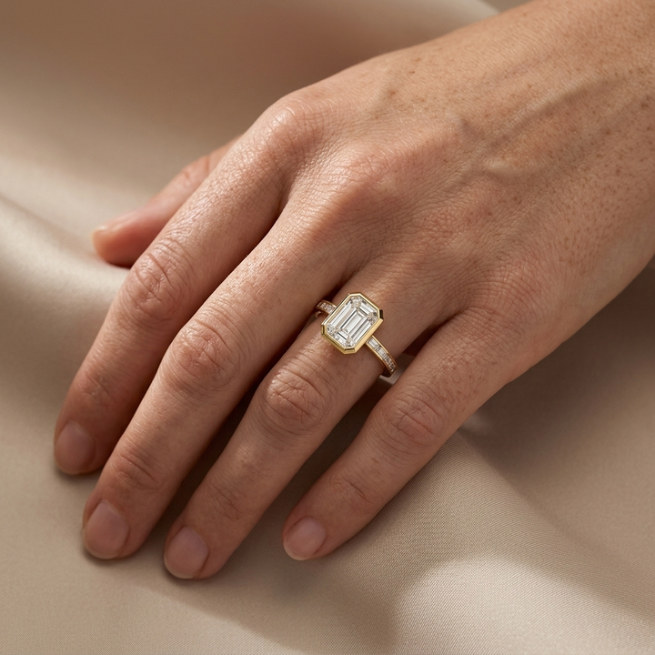 Bezel set emerald cut diamond with accented baguettes yellow gold engagement ring on woman's hand