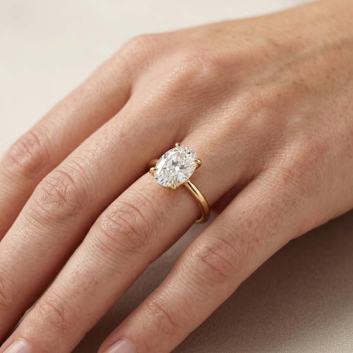 A close-up of a hand wearing a yellow gold ring with a large oval-cut clear diamond in a prong setting.