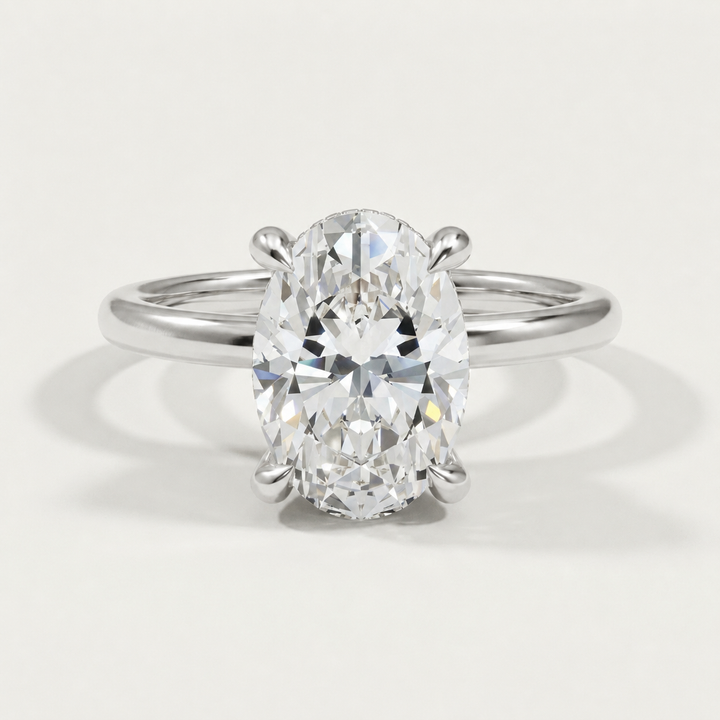 An oval-cut diamond engagement ring with diamond hidden halo set in a white gold  band, shown on a clean, light gray background.