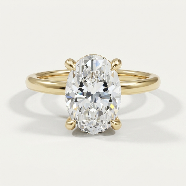 An oval-cut diamond engagement ring with diamond hidden halo in a yellow gold band with a four-prong setting, shown on a clean off-white background.