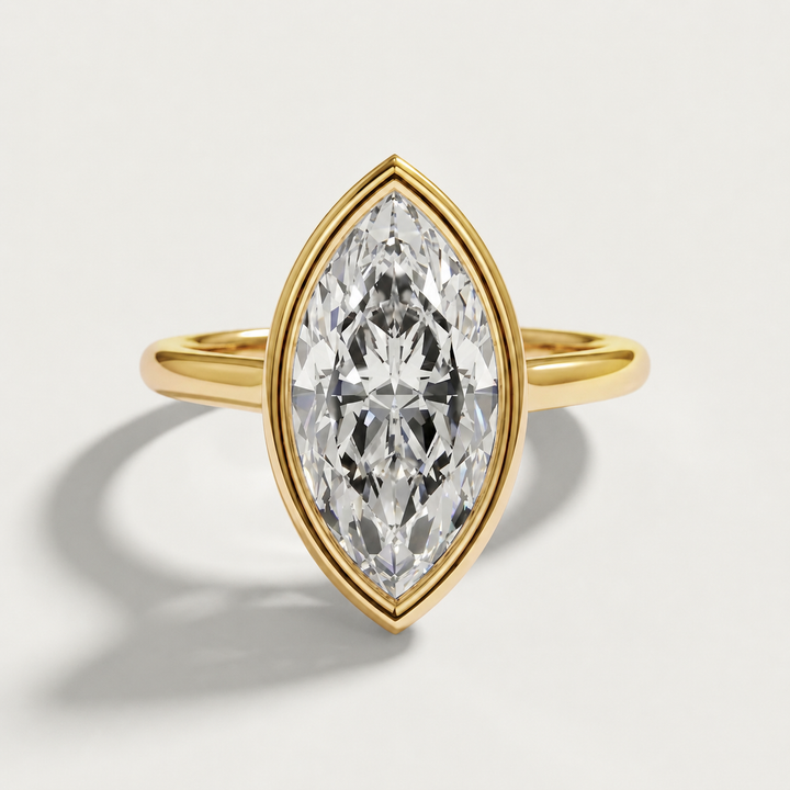 A yellow gold ring featuring a large marquise-cut clear diamond in a bezel setting, shown on a light gray background with a soft shadow.