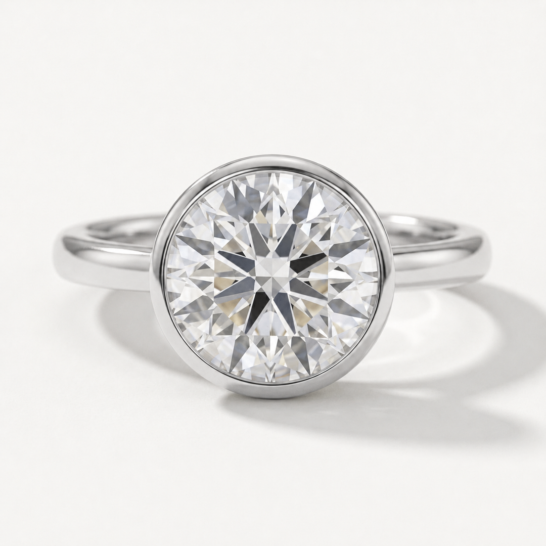 A round-cut diamond solitaire engagement ring in a polished white gold metal bezel setting, shown on a clean white background.