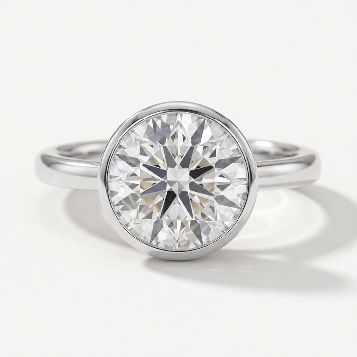 A round-cut diamond solitaire engagement ring in a polished white gold metal bezel setting, shown on a clean white background.